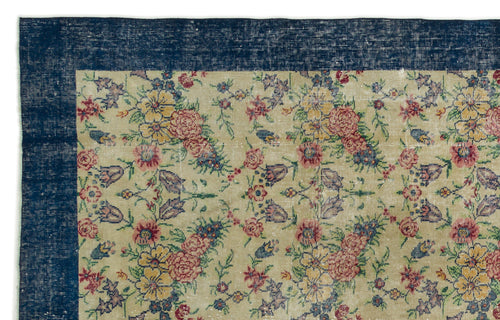 Load image 1 in gallery view. Beige rug with a distressed floral pattern in red, yellow, and blue, featuring a wide navy blue border.