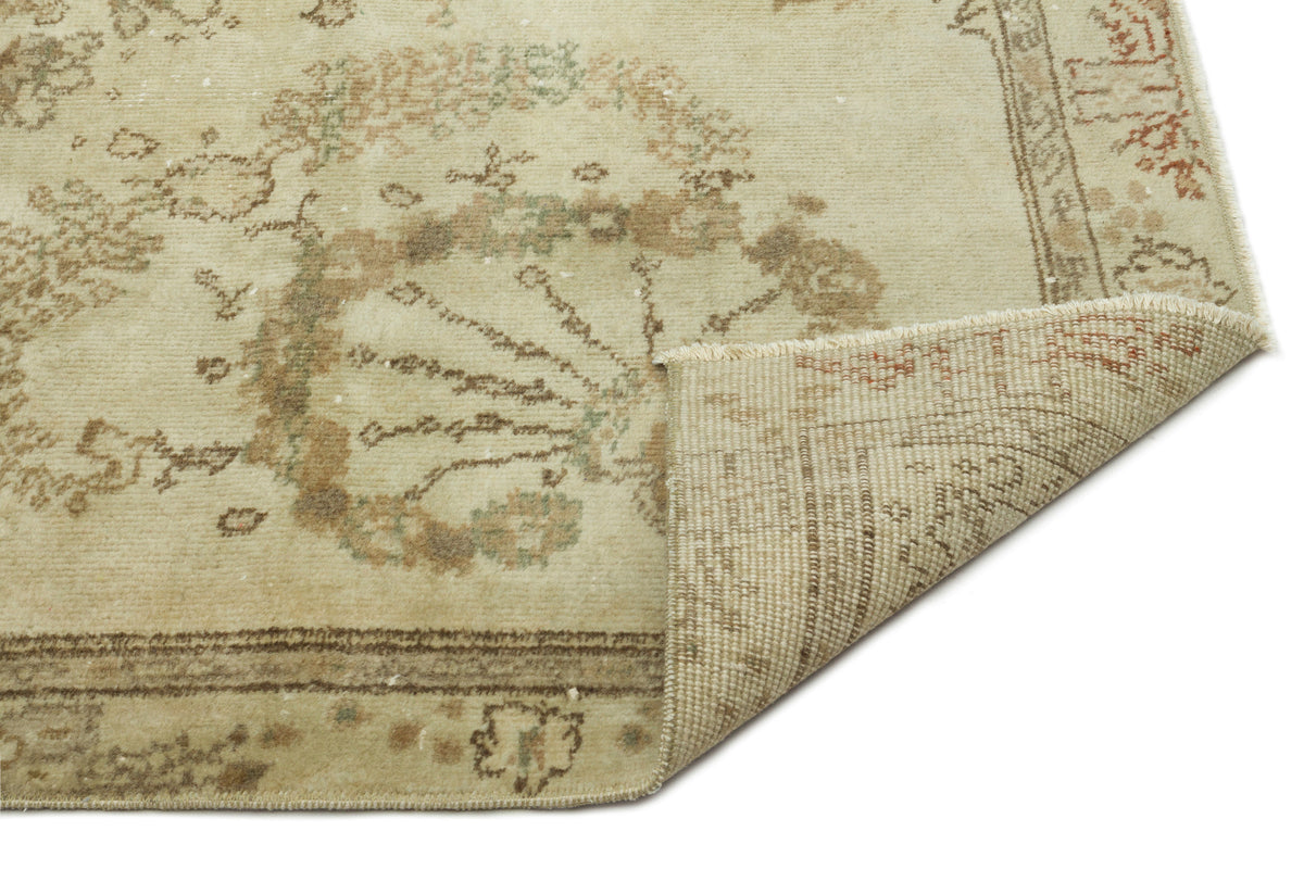 Beige vintage-style rug with a faded floral medallion pattern and a folded corner showing the woven backing.