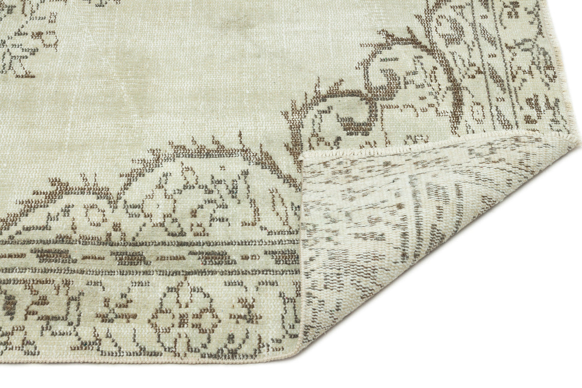 Sage green and brown distressed rug with a traditional floral medallion pattern, shown with a folded corner.