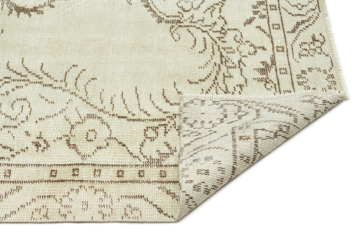 Cream and beige rug with a distressed floral medallion pattern, shown with a corner folded over on a white background.