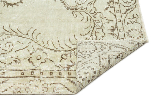 Load image 1 in gallery view. Cream and beige rug with a distressed floral medallion pattern, shown with a corner folded over on a white background.