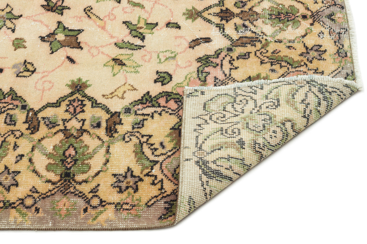 Beige vintage-style rug with green, pink, and brown floral medallion patterns, shown with a corner folded over.