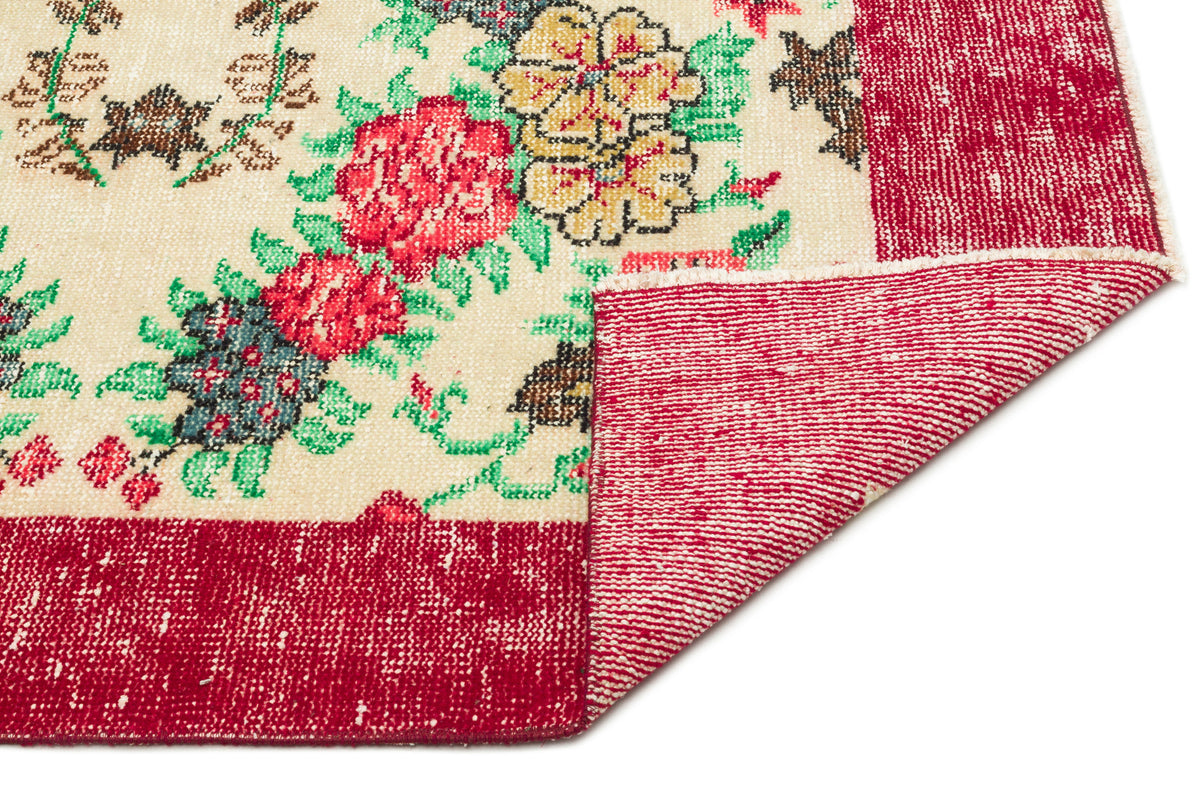 Cream rug with red, yellow, and green floral pattern and a wide red border, shown with a corner folded over.