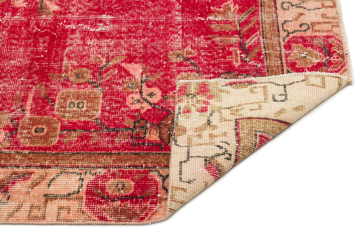 Distressed red and beige vintage-style rug with a floral medallion pattern, showing a folded corner on a white background.
