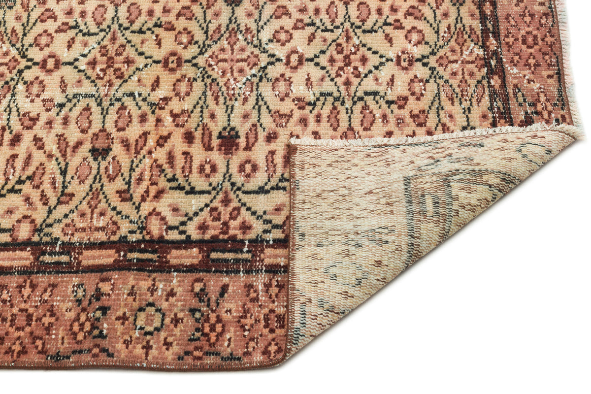 Distressed terracotta and beige rug with a traditional floral lattice pattern and a folded corner showing the backing.