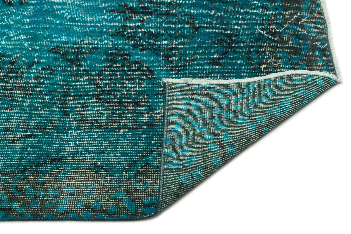 Teal and black distressed floral rug with a folded corner revealing the woven backing.