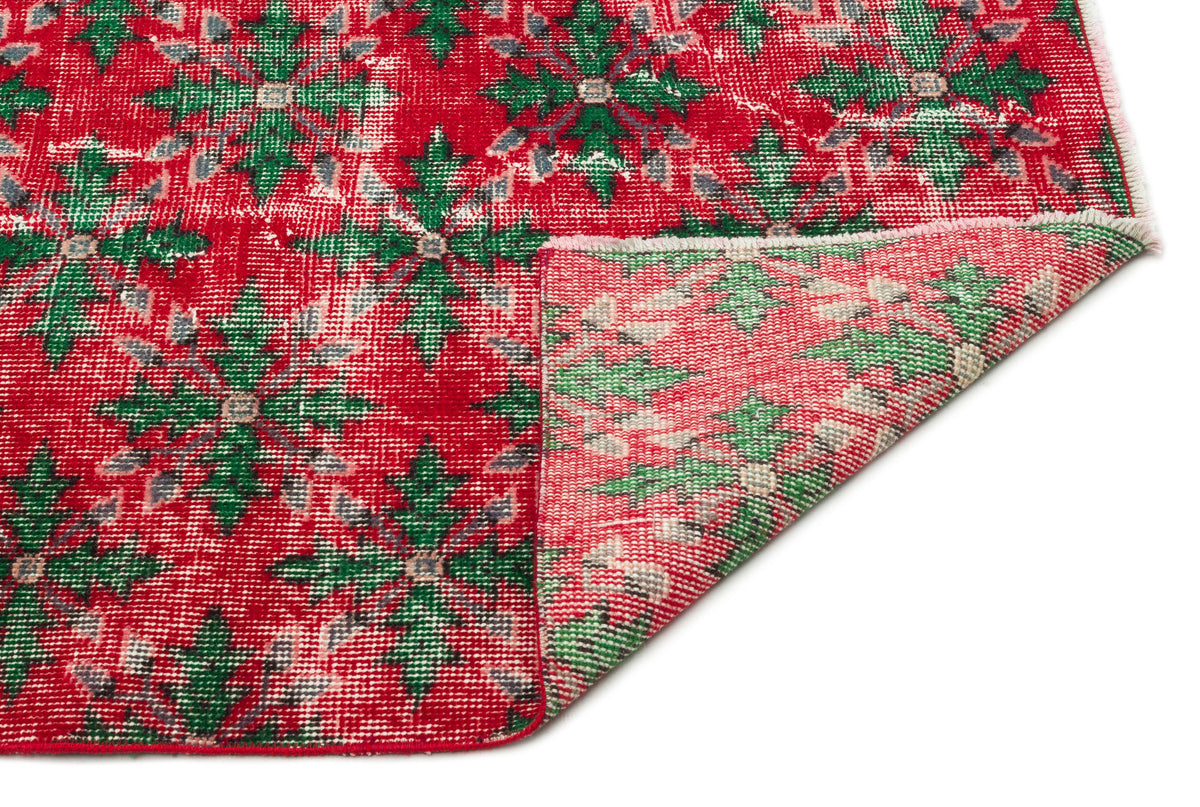 Red and green distressed floral medallion rug with a folded corner showing the woven backing.