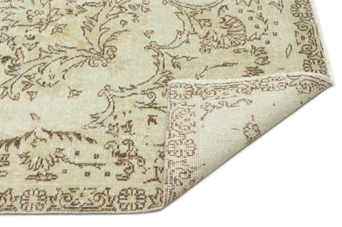 Load image 1 in gallery view. Beige and brown distressed rug with a traditional floral medallion pattern, shown with a folded corner on white.