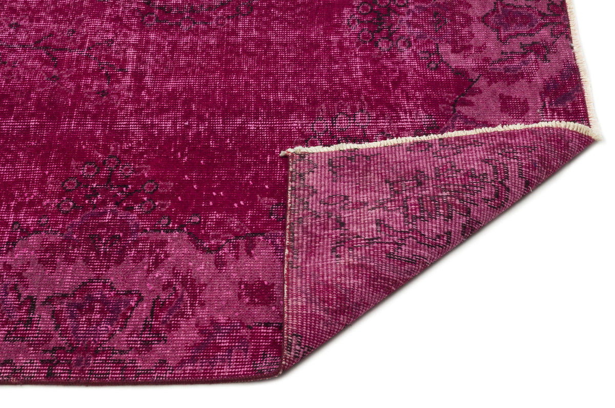 Magenta distressed rug with a faded floral medallion pattern and a folded corner showing the woven backing.