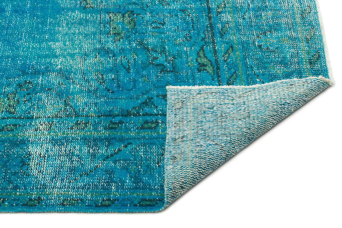 Distressed turquoise and teal rug with a faded traditional pattern, shown with a corner folded to reveal the backing.