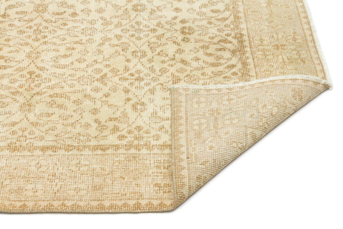 Beige and cream traditional rug with a faded floral medallion pattern and a folded corner showing the woven backing.