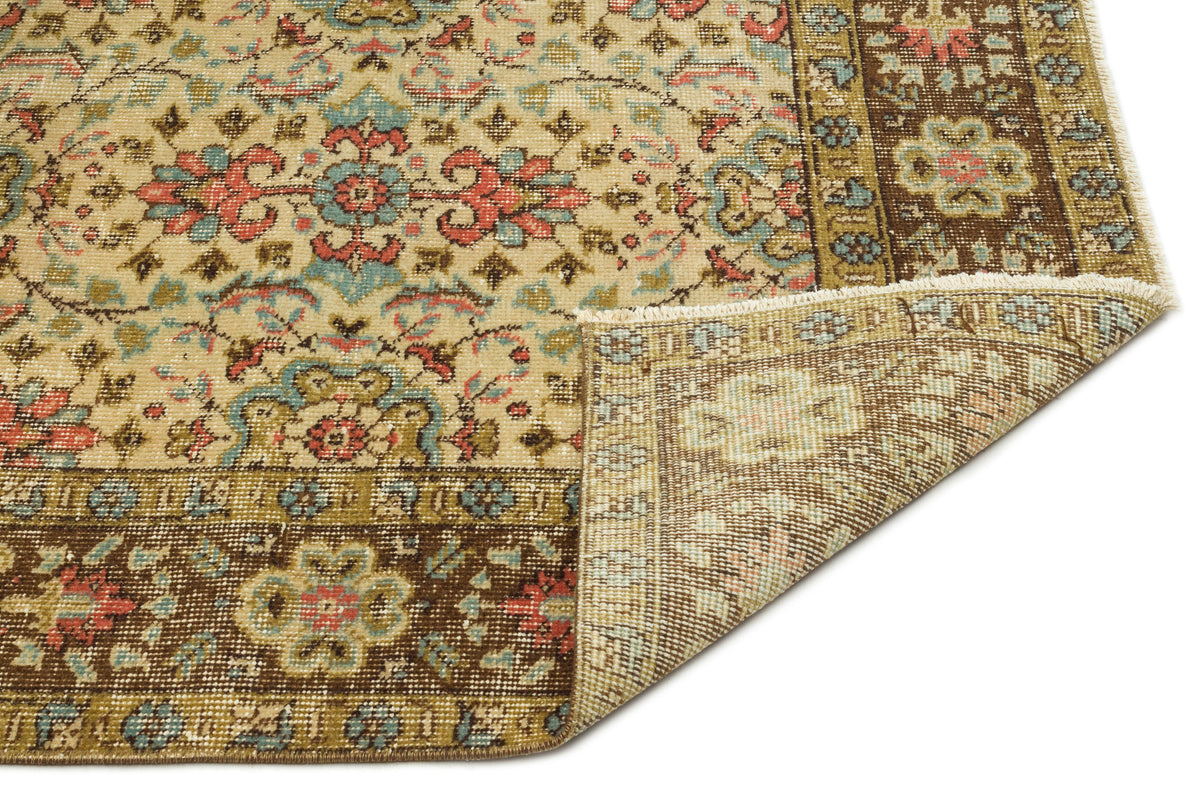 Beige traditional rug with a floral medallion pattern in red, blue, and brown, shown with a folded corner.