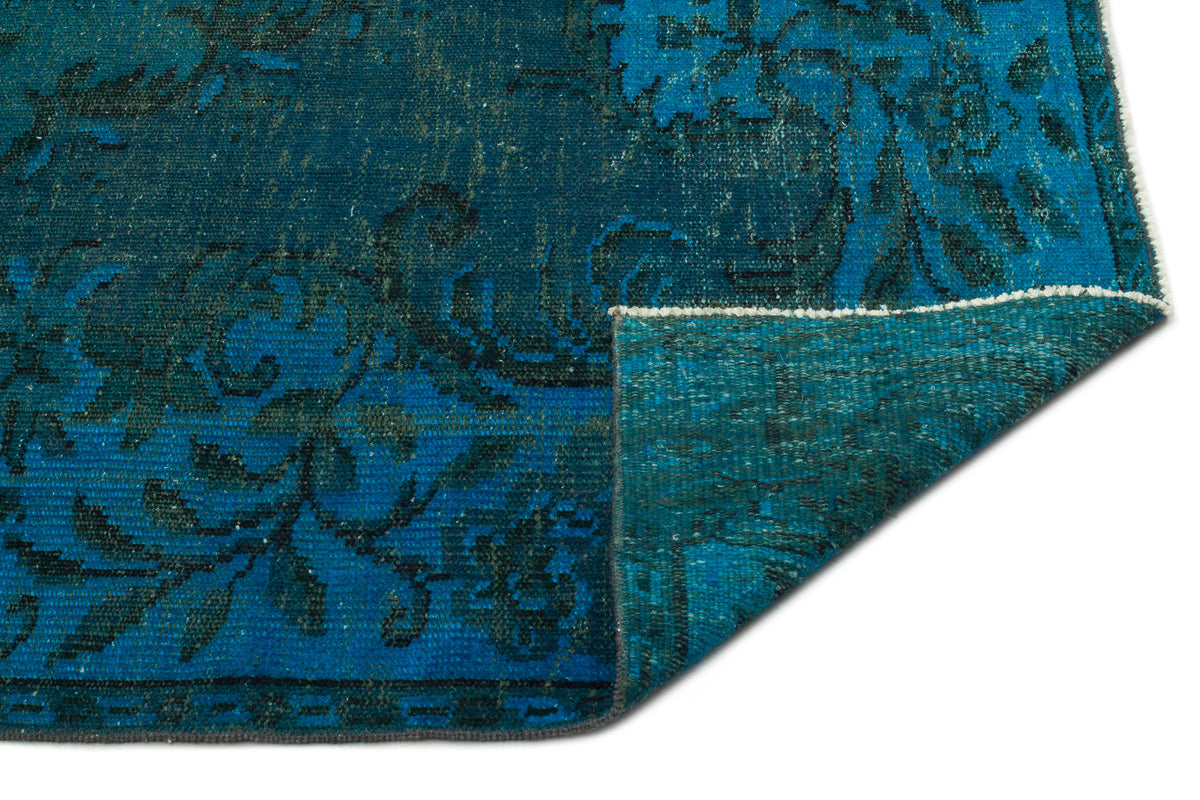 Teal and dark blue distressed rug with a traditional floral pattern, shown with a corner folded over on a white background.