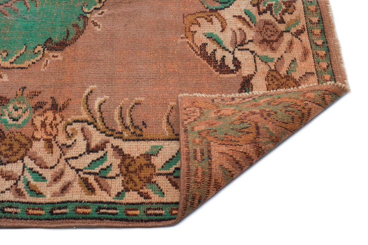 Distressed terracotta rug with green and brown floral medallion patterns and a folded corner, isolated on white.