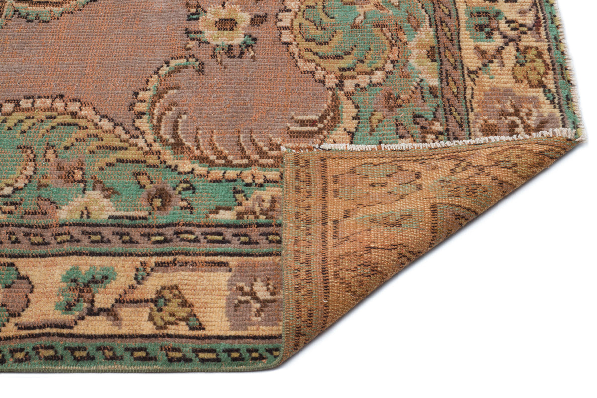 Distressed vintage-style rug in mauve, teal, and tan with a floral medallion pattern, shown with a folded corner.