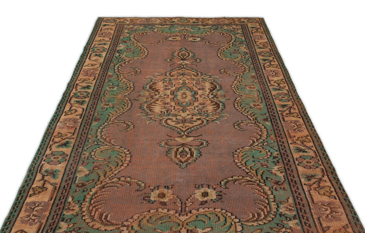 Distressed mauve, green, and tan vintage-style rug with a central floral medallion and ornate border on a white background.
