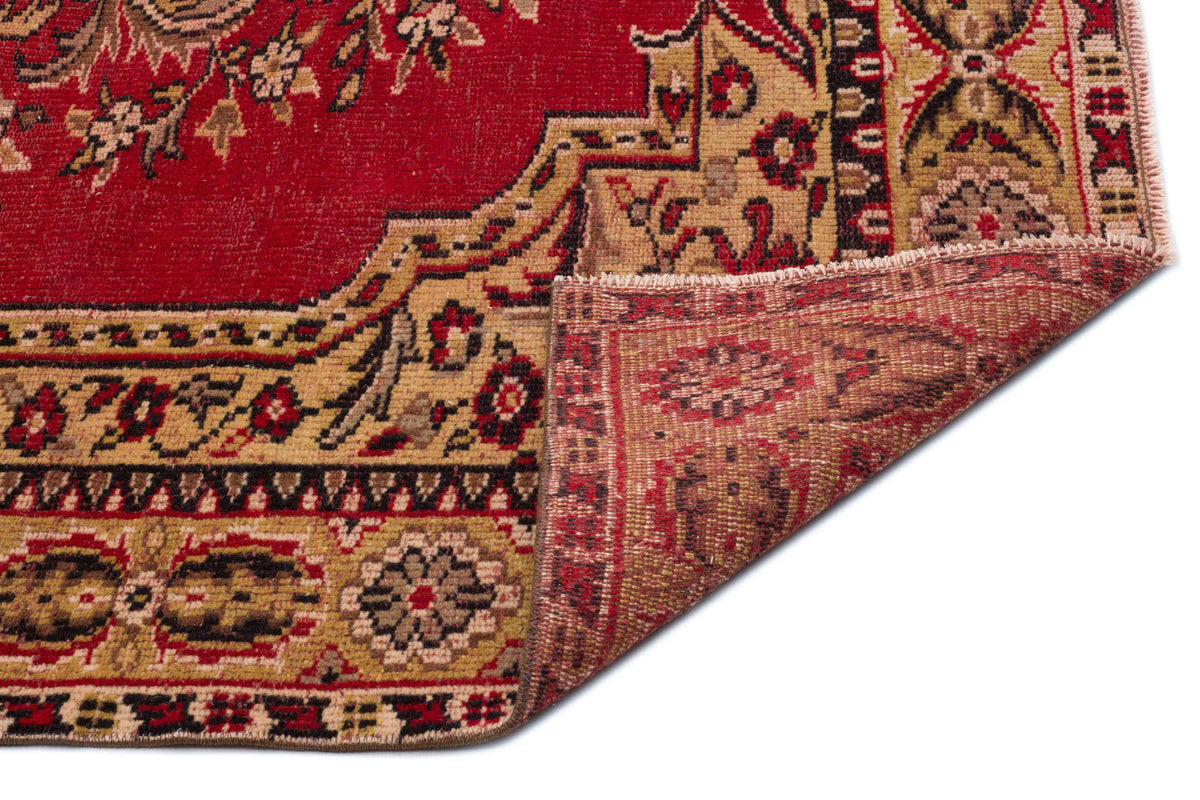Red and tan traditional rug with a floral medallion pattern, shown with a corner folded over on a white background.
