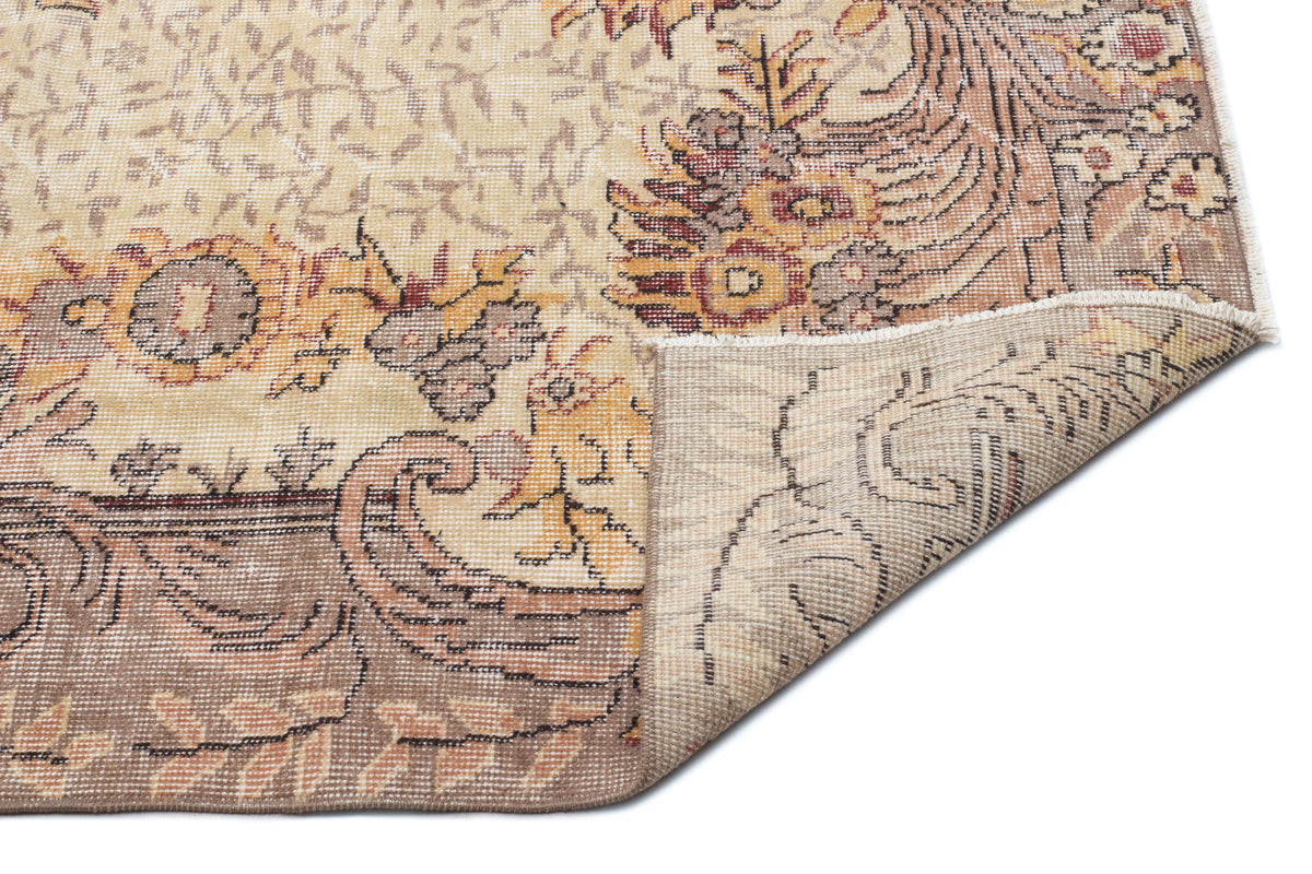 Beige and brown traditional rug with a floral medallion pattern, shown with a corner folded over on a white background.