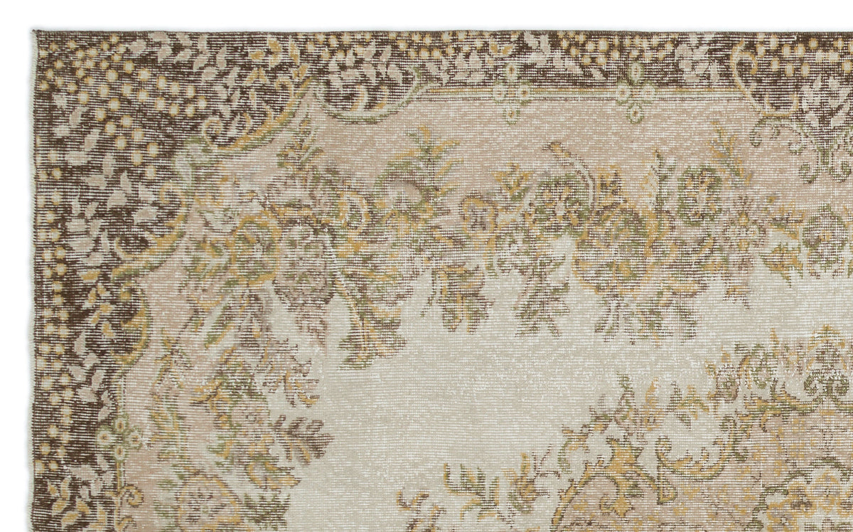 Distressed beige rug with a dark brown border and faded floral medallion pattern in olive green and mustard yellow.