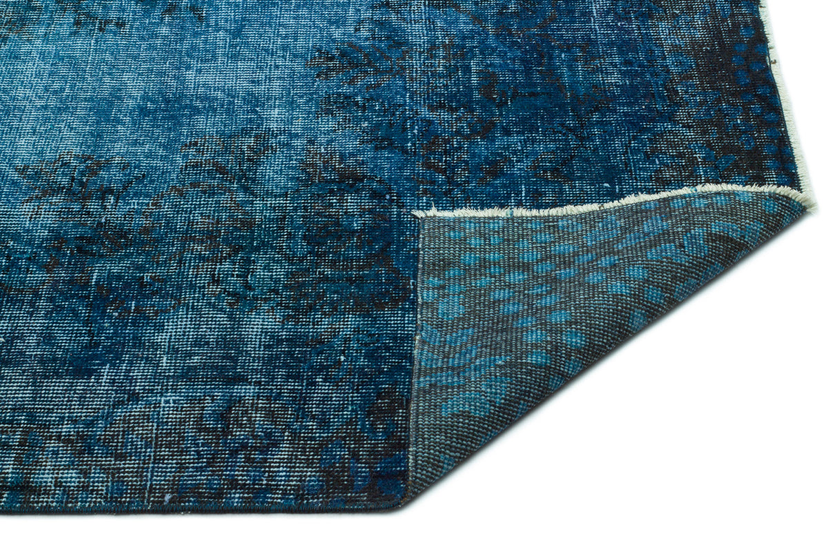 Distressed blue and black vintage-style rug with a folded corner revealing the grey woven backing.