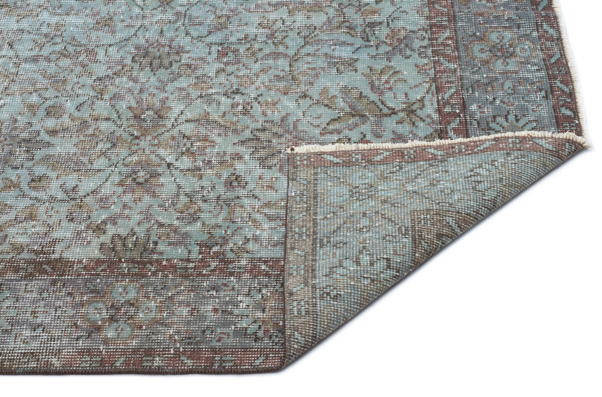 Distressed blue and brown traditional floral rug with a folded corner revealing the underside on a white background.