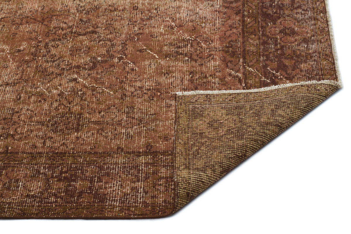 Distressed brown and tan traditional rug with a faded medallion pattern and a folded corner showing the woven backing.
