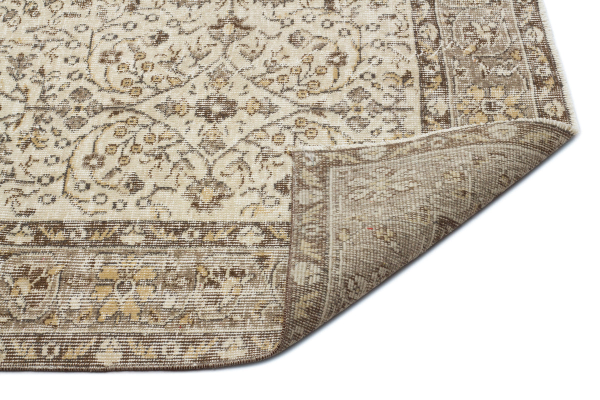 Beige and brown traditional floral rug with a folded corner revealing the woven backing on a white background.