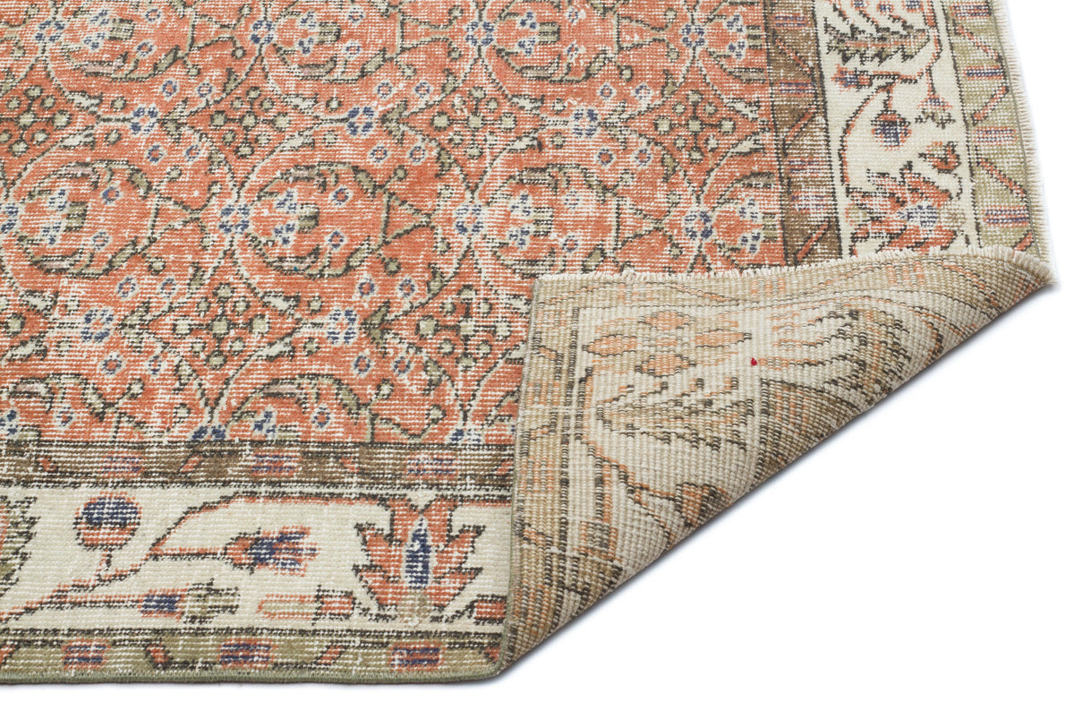 Terracotta and cream traditional rug with a floral medallion pattern and a folded corner showing the woven backing.