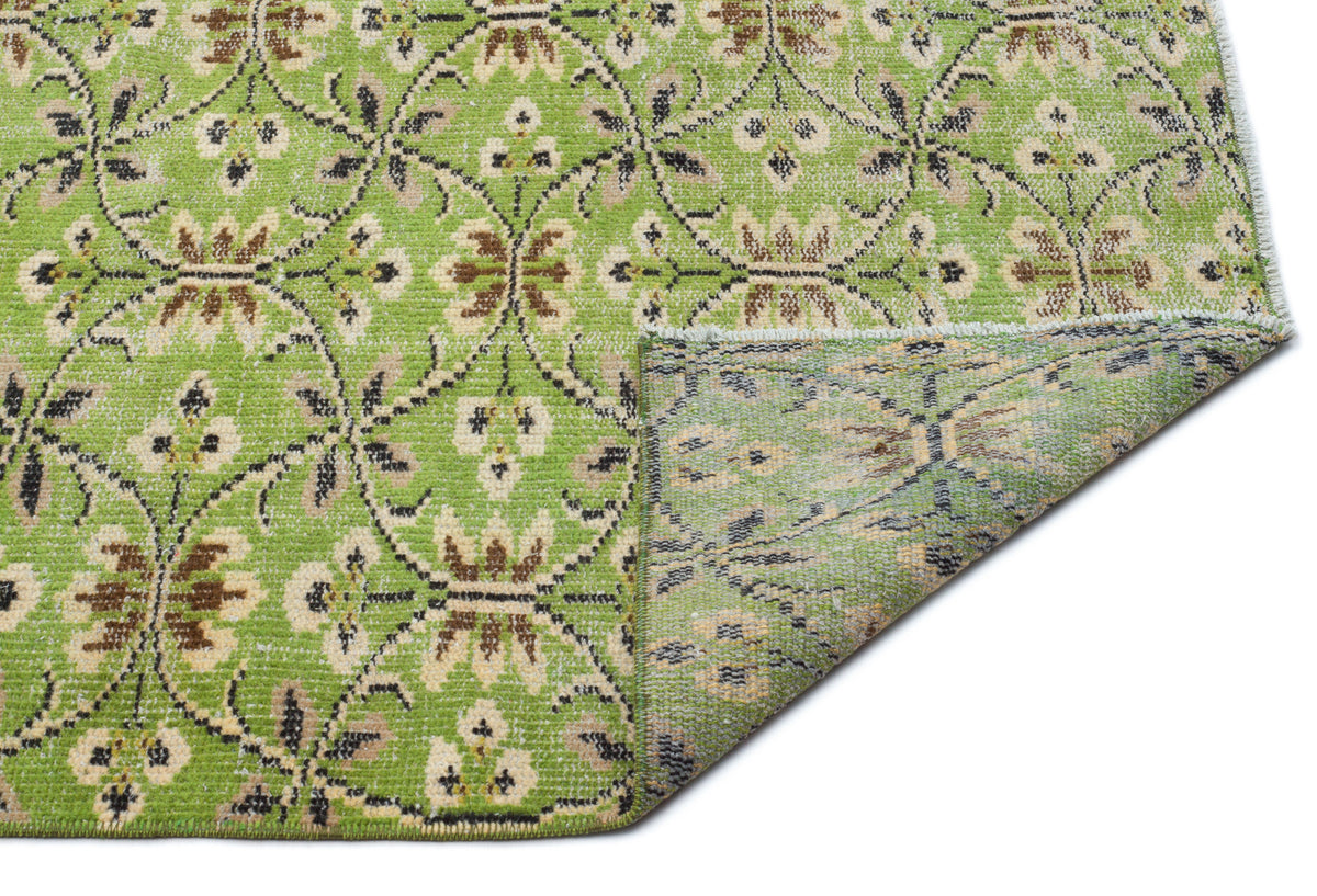 Lime green rug with a brown and cream floral trellis pattern, shown with a corner folded over on a white background.