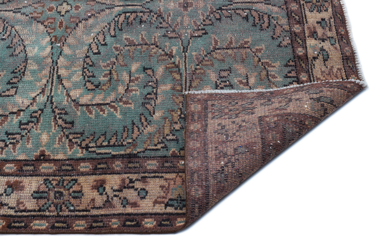 Teal and brown traditional rug with a floral medallion pattern, shown with a corner folded over on a white background.