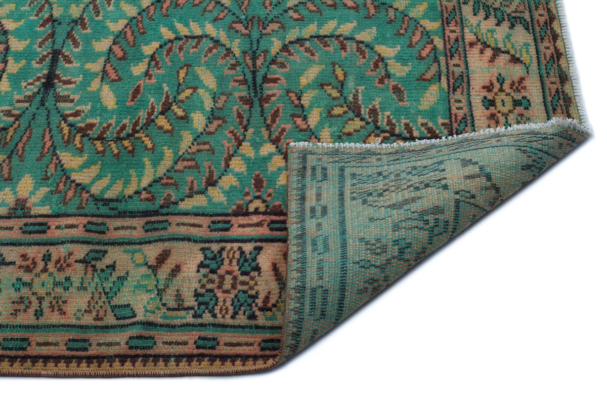 Teal and beige vintage-style rug with a floral vine pattern and a folded corner revealing the woven backing.