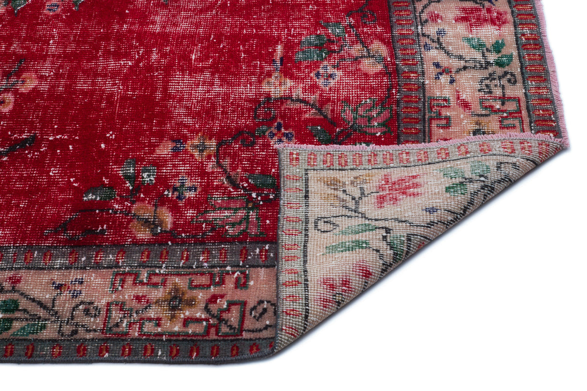 Distressed red rug with a floral pattern, beige border, and a folded corner revealing the underside.