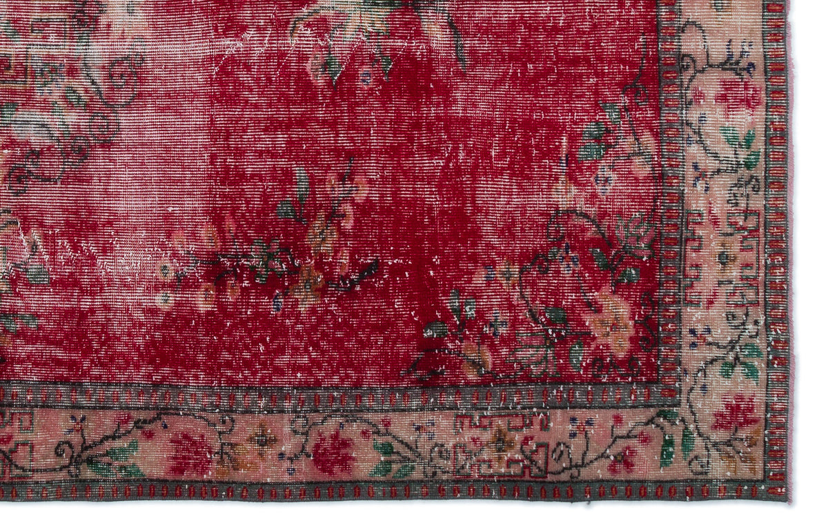 Distressed red rug with a floral pattern and a beige border featuring intricate botanical motifs.