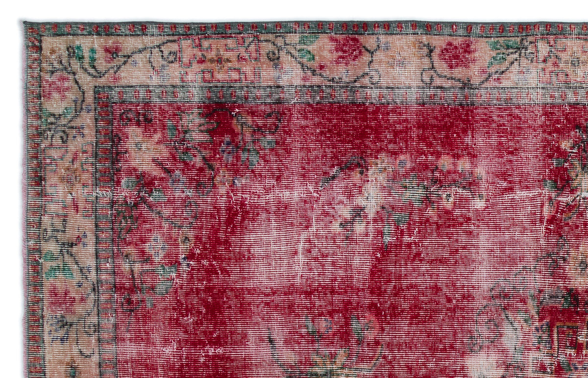Distressed red rug with a floral border in cream, green, and black, featuring a faded, vintage-style woven texture.