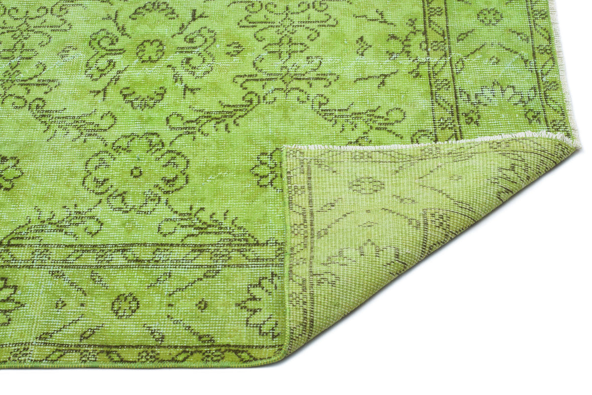 Bright lime green rug with a distressed dark olive floral medallion pattern and a folded corner on a white background.