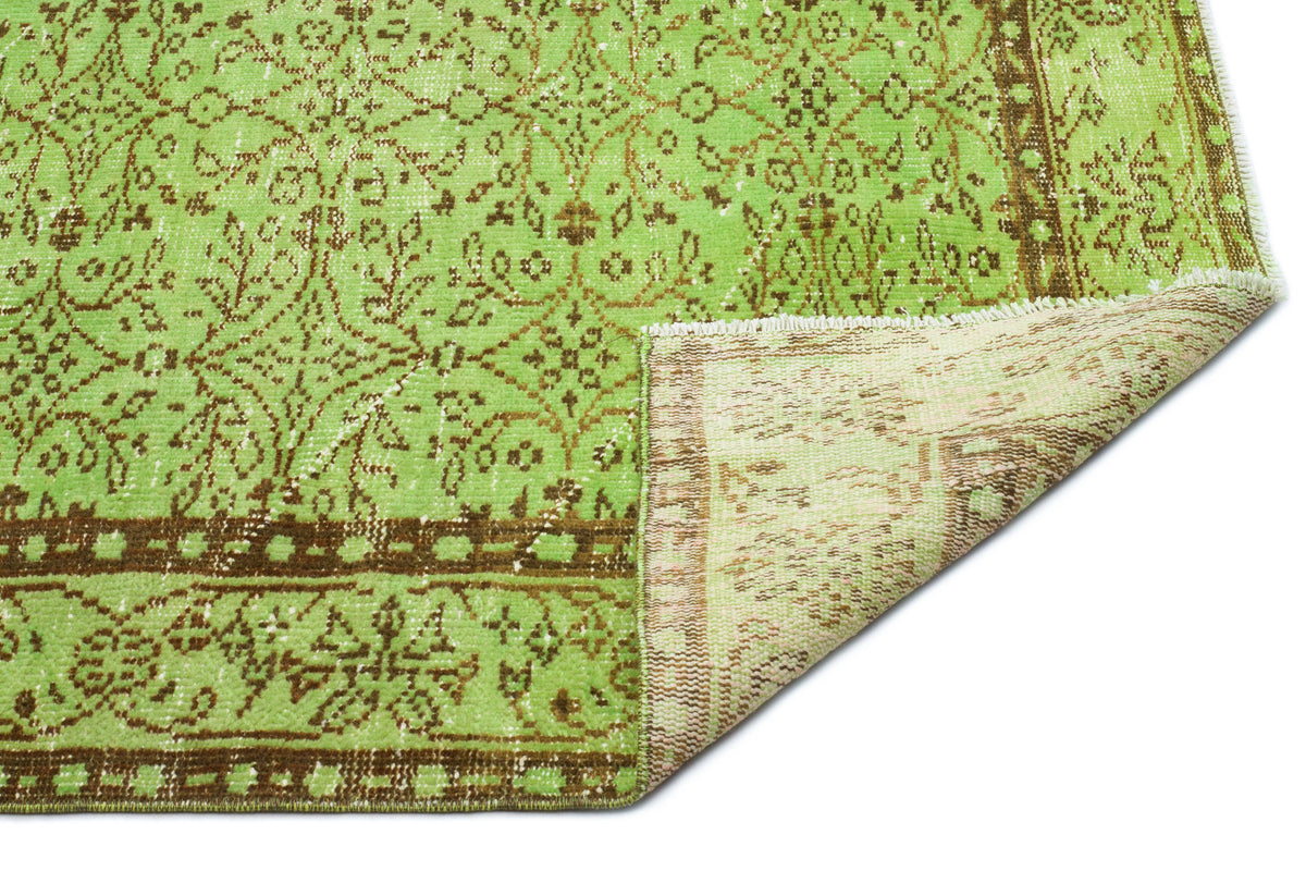 Lime green and brown vintage-style rug with a distressed floral medallion pattern and a folded corner showing the backing.