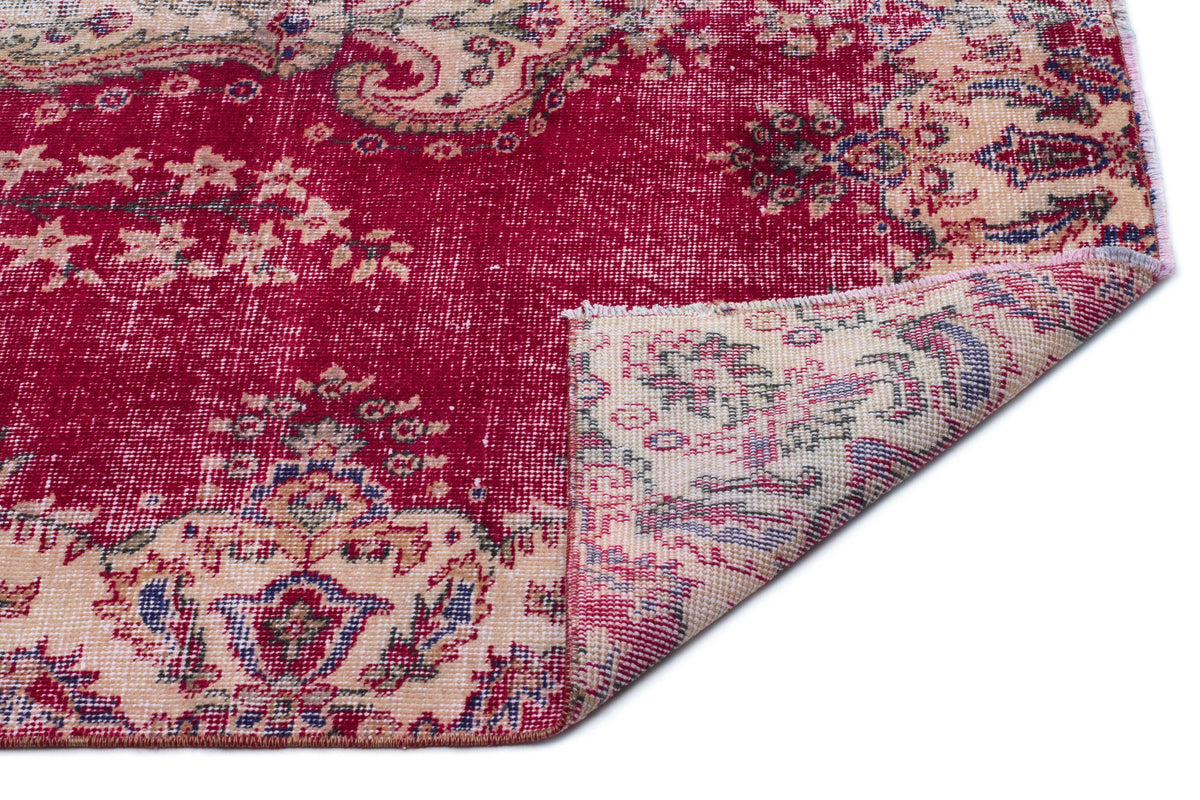 Distressed crimson and beige rug with a traditional floral medallion pattern, shown with a corner folded over.