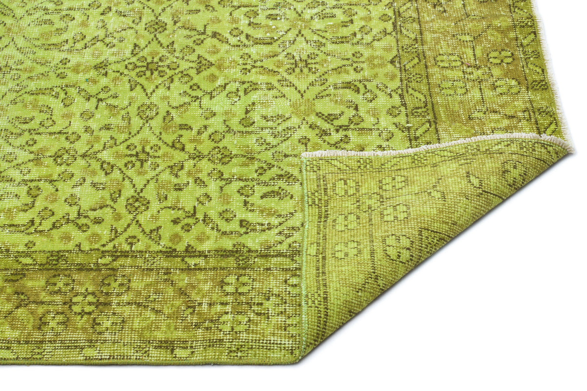 Chartreuse and olive green vintage-style rug with a distressed floral medallion pattern and a folded corner.