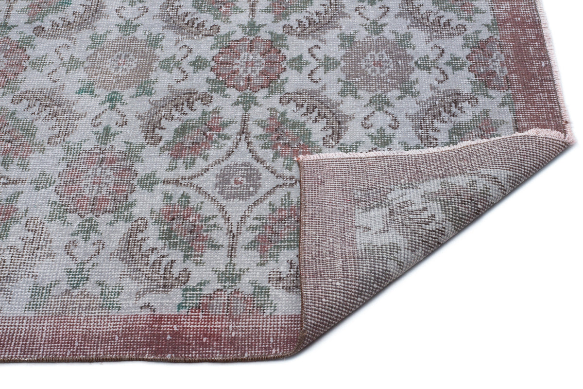 Distressed floral medallion rug in muted sage, rose, and cream with a folded corner revealing the woven backing.