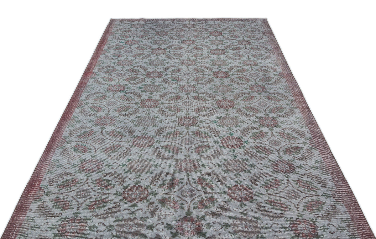 Distressed grey rug with a repeating floral medallion pattern in muted red and green, isolated on a white background.