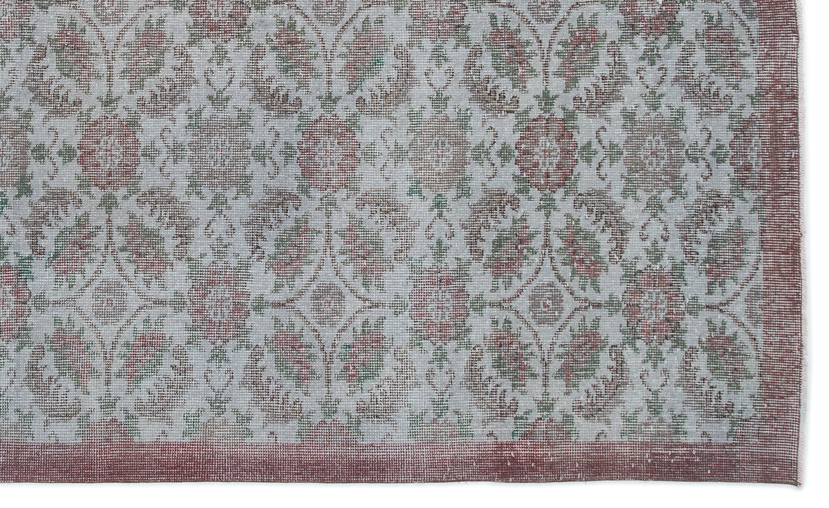 Light gray rug with a faded floral medallion pattern in muted red and green, featuring a solid red border.