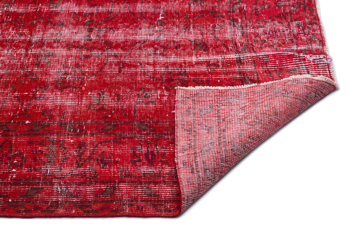 Distressed red vintage-style rug with a faded floral pattern and a folded corner showing the woven backing.