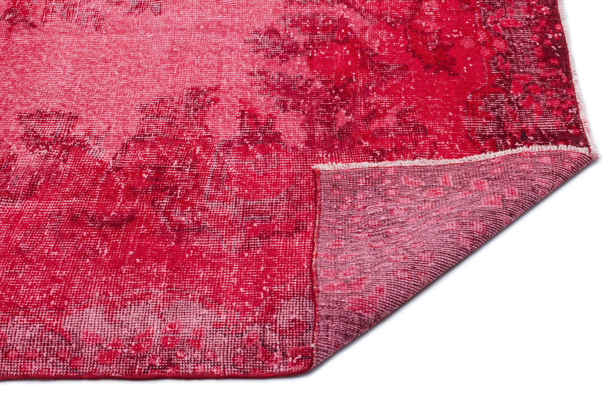 Distressed crimson and magenta rug with a faded floral pattern, shown with a corner folded over on a white background.