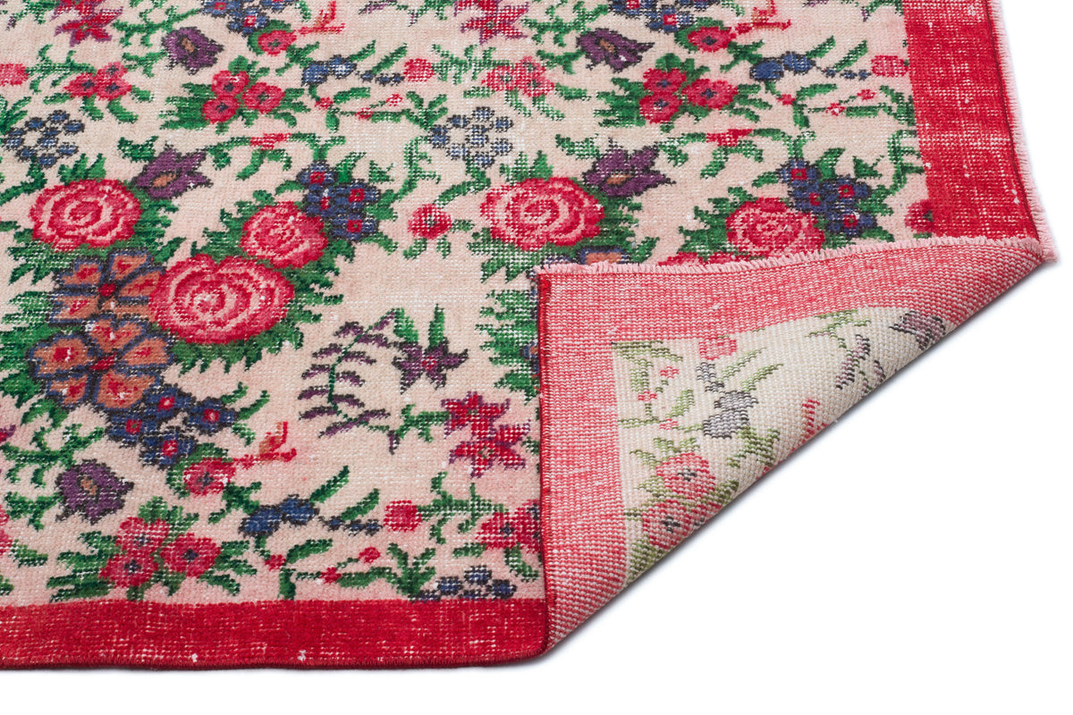 Beige rug with a red, green, and purple floral pattern and a folded corner revealing the underside.