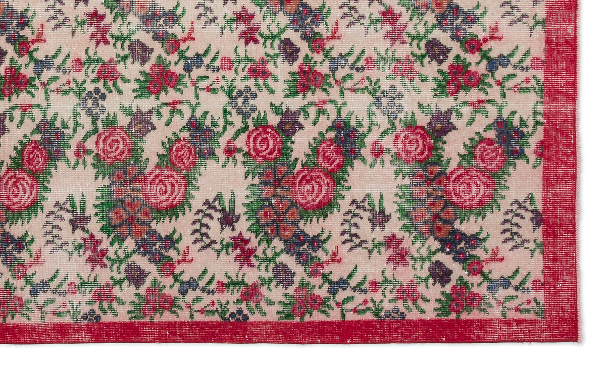 Beige rug with a repeating floral pattern in red, green, and purple, featuring a solid red border.