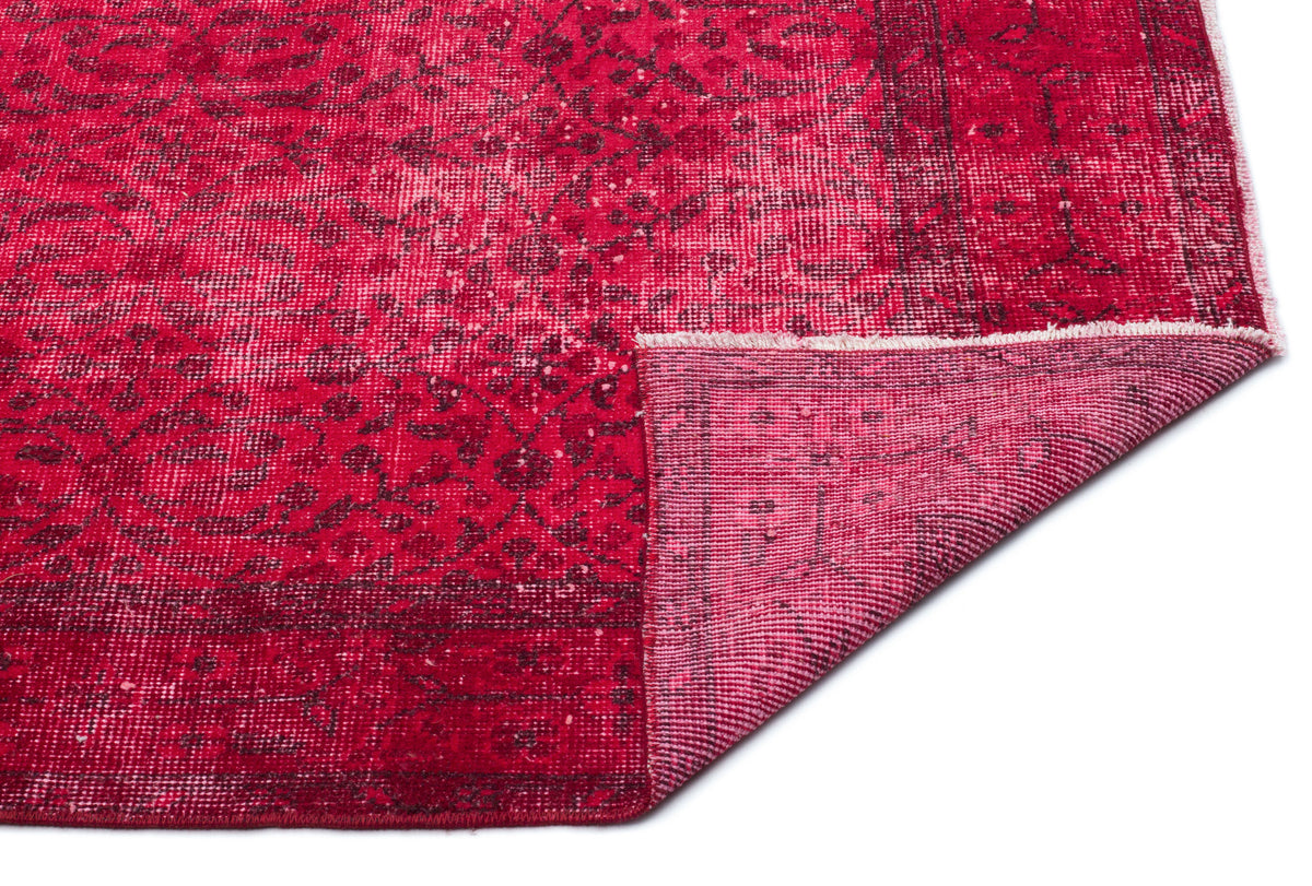 Distressed crimson rug with a dark floral pattern and a folded corner revealing the woven backing.