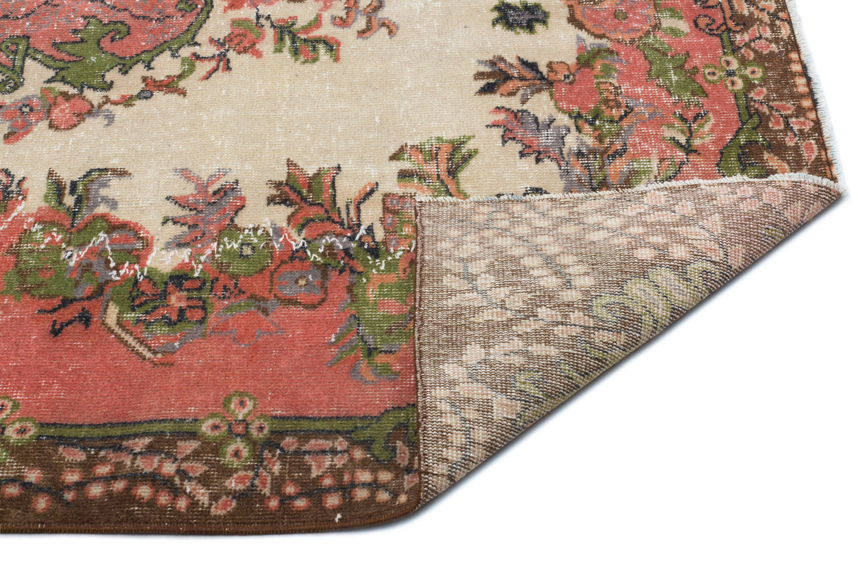 Distressed beige rug with a floral medallion pattern in coral, green, and brown, showing the woven backing.