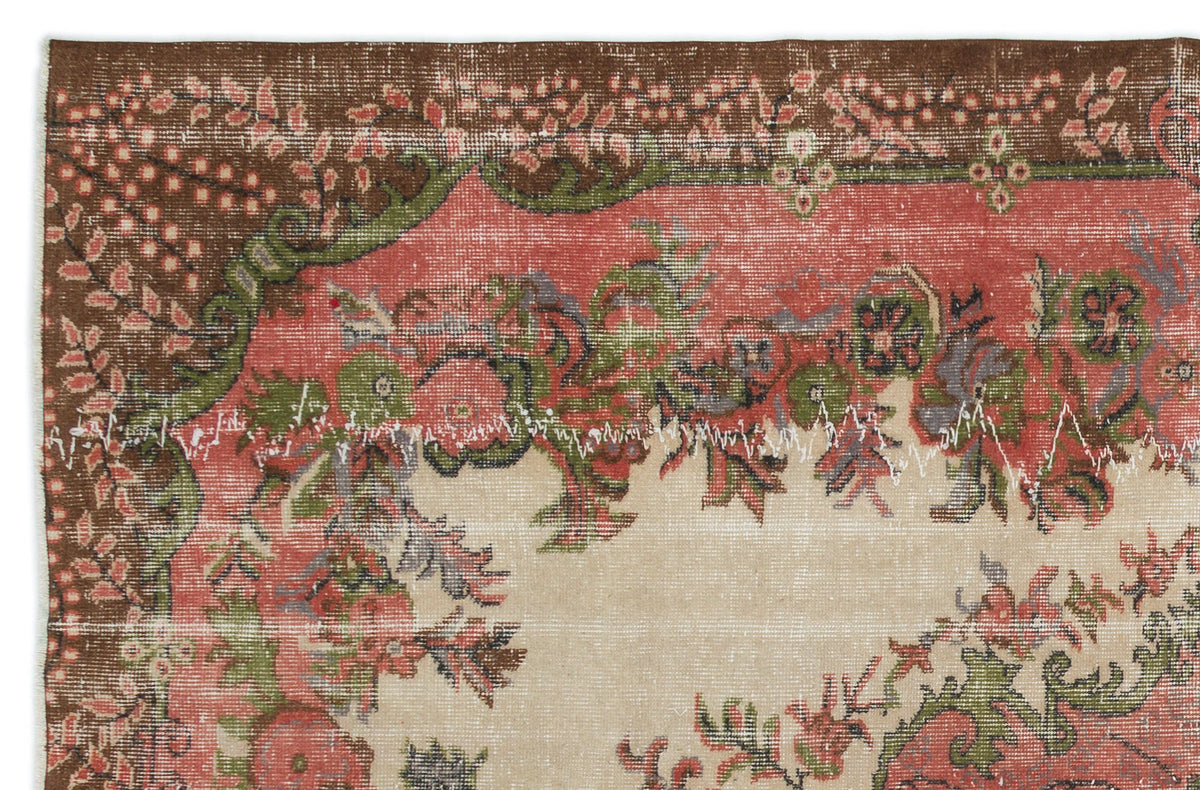 Distressed vintage rug fragment with a floral medallion pattern in brown, coral, and sage green on a cream background.