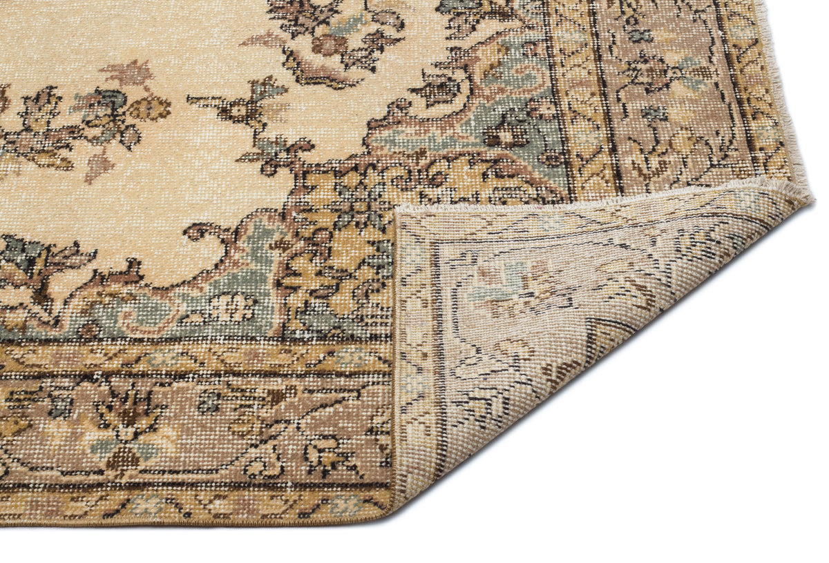Beige and sage green vintage-style rug with a floral medallion pattern, shown with a corner folded over.