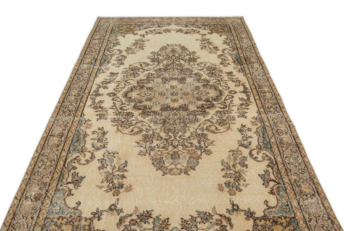 Beige traditional rug with a central floral medallion and intricate border in muted brown, blue, and cream tones.